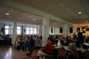 sitzende Teilnehmer Arbeitskreis in Saal und ein stehender Redner